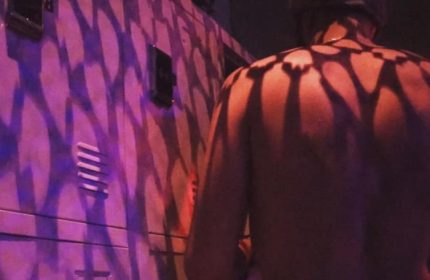 Depot Milano gay travel: Shirtless man stands near a wall with purple lighting and shadow patterns. Gay nightlife in Milan, Italy.
