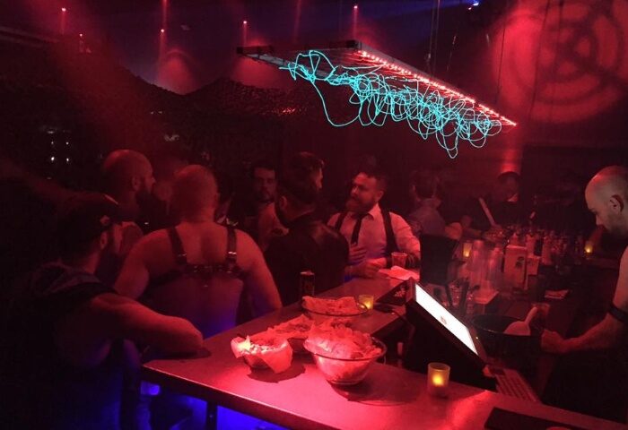Depot Milano: Gay bar scene with men at the bar, red lighting, and unique light fixture. Milan gay nightlife travel advice.