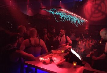 Depot Milano: Gay bar scene with men at the bar, red lighting, and unique light fixture. Milan gay nightlife travel advice.