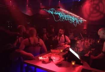 Depot Milano: Gay bar scene with men at the bar, red lighting, and unique light fixture. Milan gay nightlife travel advice.