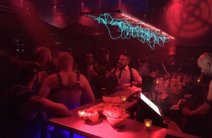 Depot Milano: Gay bar scene with men at the bar, red lighting, and unique light fixture. Milan gay nightlife travel advice.