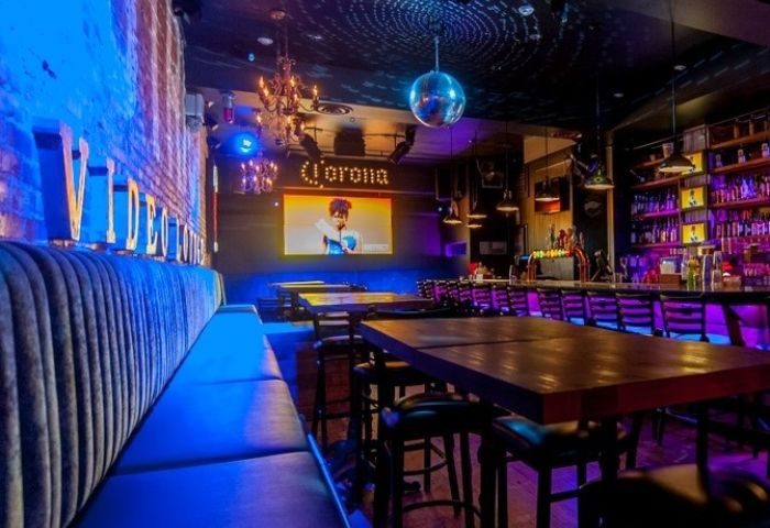 District Video Lounge, a gay bar in Montreal. Blue lighting, video screen, bar, tables, and seating. Nightlife for gay men travelers.