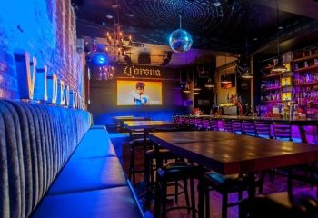 District Video Lounge, a gay bar in Montreal. Blue lighting, video screen, bar, tables, and seating. Nightlife for gay men travelers.