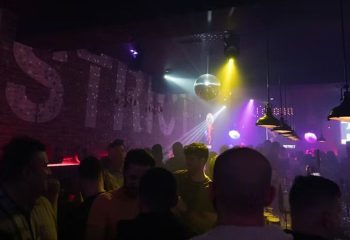 District Video Lounge, a gay bar in Montreal. Crowded dance floor with disco ball and stage. Purple and yellow lights illuminate the scene.