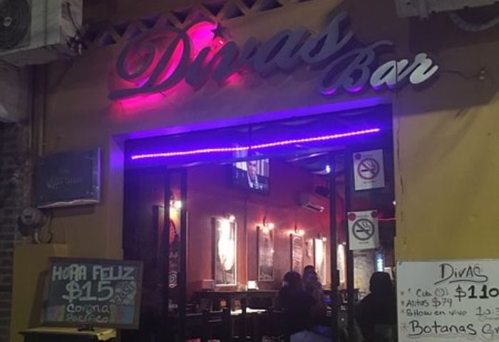 Diva's Gay Bar in Puerto Vallarta. Exterior view with neon sign, happy hour specials, and patrons inside. A popular gay travel destination.