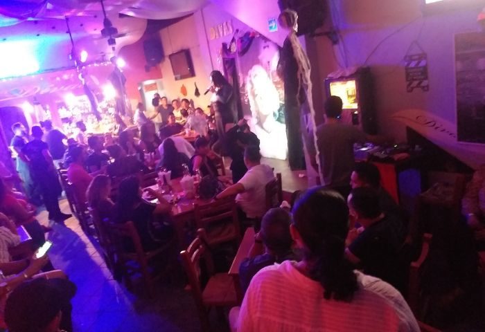 Gay nightlife at Diva's Gay Bar in Puerto Vallarta. A singer performs on stage in a crowded, lively gay bar with colorful lighting.
