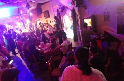 Gay nightlife at Diva's Gay Bar in Puerto Vallarta. A singer performs on stage in a crowded, lively gay bar with colorful lighting.