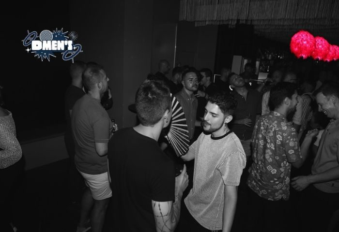 Dmen's Gay Bar in Barcelona: Gay men dancing in a dark club with red lights. Nightlife scene, travel advice for gay visitors.