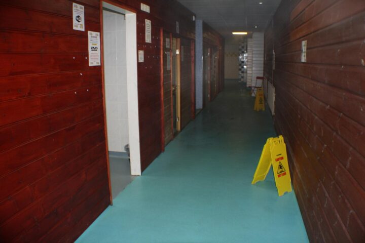 E15 Club Gay Sauna interior. Hallway view with wooden walls, blue floor, and caution signs. Gay sauna travel advice.