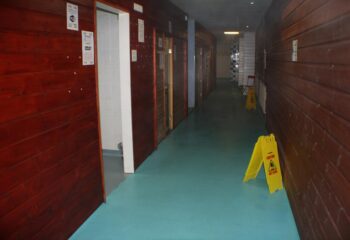 E15 Club Gay Sauna interior. Hallway view with wooden walls, blue floor, and caution signs. Gay sauna travel advice.