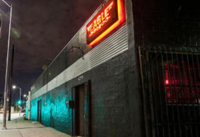 Night shot of Eagle LA, a gay bar. Neon sign glows above the entrance. A popular spot for gay men's travel in Los Angeles.