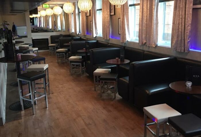 Interior of EVA Manchester, a gay bar. Black leather booths, stools, wood floors, and decorative lighting create a stylish atmosphere. Gay travel advice.