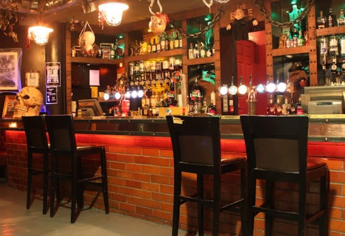 Interior of Eagle Manchester, a gay bar. Brick bar with stools, shelves of liquor bottles, and Halloween decorations. Nightlife.
