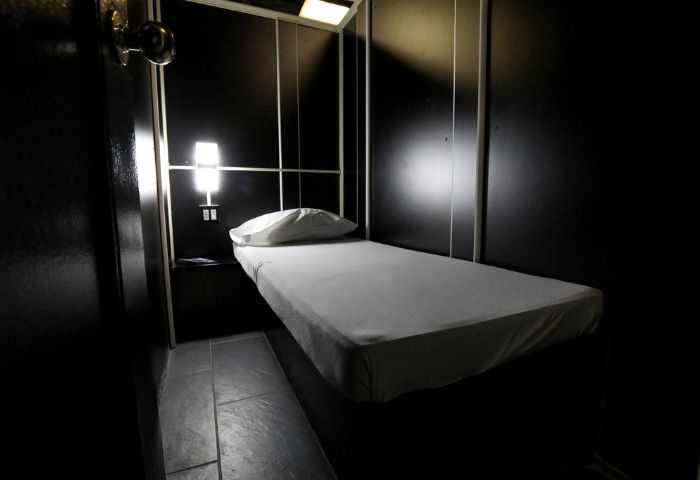 East Side Club, New York gay sauna. A private room with a bed, pillow, and nightstand. Dark walls and dim lighting create an intimate atmosphere.