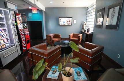 East Side Club, New York gay sauna lounge area. Brown leather chairs, vending machines, TV, and artwork. Relaxing space for gay men's travel.
