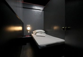 East Side Club, New York gay sauna. Private room with bed, pillows, towels, and dim lighting. A dark, intimate space for relaxation.