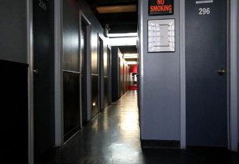 Hallway view inside East Side Club, a gay sauna in New York. Dark lockers line the walls, with a 'No Smoking' sign visible. Gay travel.