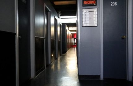 Hallway view inside East Side Club, a gay sauna in New York. Dark lockers line the walls, with a 'No Smoking' sign visible. Gay travel.