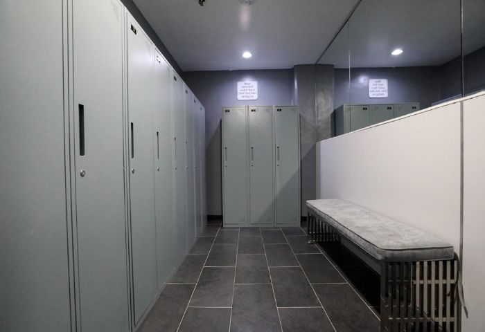 East Side Club, a gay sauna in New York: Locker room with gray lockers, dark tile floor, bench, and mirror. Men's travel advice.