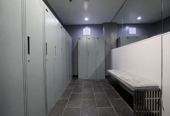 East Side Club, a gay sauna in New York: Locker room with gray lockers, dark tile floor, bench, and mirror. Men's travel advice.