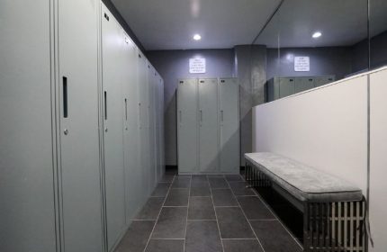 East Side Club, a gay sauna in New York: Locker room with gray lockers, dark tile floor, bench, and mirror. Men's travel advice.