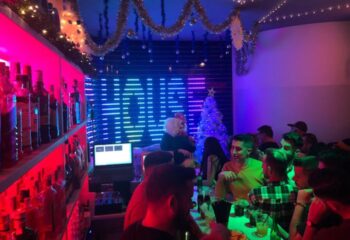 Eden Nightclub, a gay club in Torremolinos, Spain, with a festive atmosphere. Patrons enjoy drinks at the bar under colorful lights.
