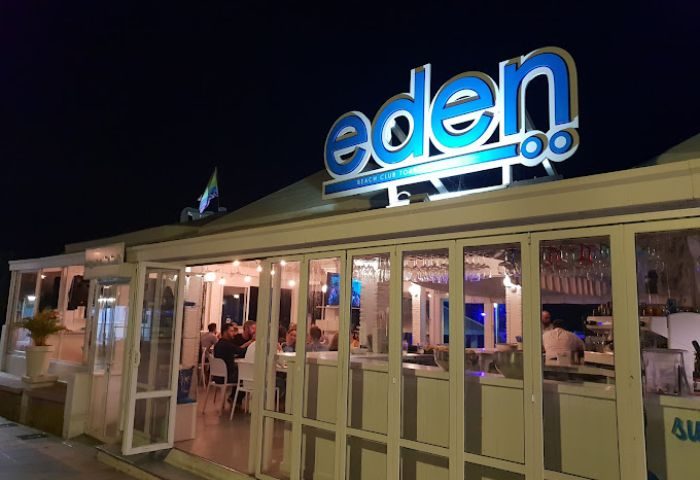 Exterior of Eden Nightclub, a gay beach club in Torremolinos, Spain. Lit up at night with a rainbow flag on the roof. Outdoor dining.