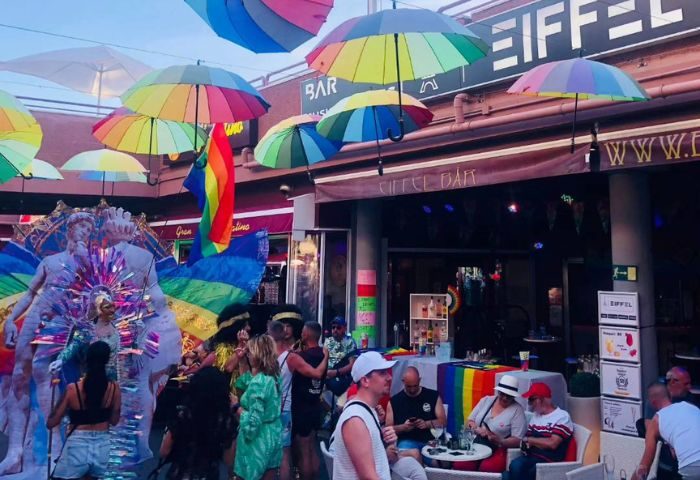 Eiffel Bar, a vibrant gay bar in Gran Canaria. Rainbow umbrellas decorate the exterior. Patrons enjoy drinks, celebrating Pride. Gay travel.