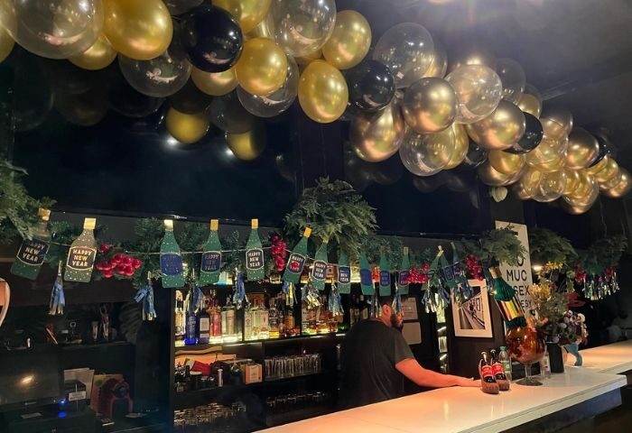 Madrid's El-12 Club gay bar interior. Balloons, New Year's decorations, and a bartender behind the counter. Gay travel advice.