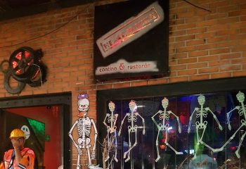 El Almacen Gay Bar in Mexico. Halloween decor, skeletons adorn the entrance. A man in a construction outfit stands nearby. Gay travel.