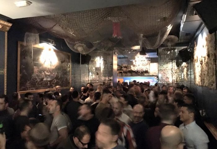 Crowded interior of El Cangrejo, a gay bar in Barcelona's Eixample district. Men are standing close together, with nautical decor overhead.