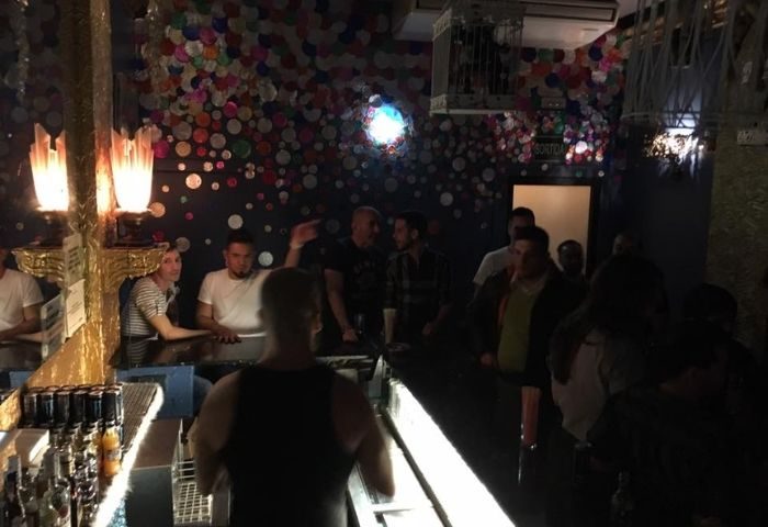 Interior of El Cangrejo, a gay bar in Barcelona's Eixample district. The bar is crowded with patrons. Colorful decor.