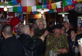 El Horno Gay Bar in Sitges: A lively scene inside, with people in costumes, colorful decorations, and a drag queen. Gay travel advice.