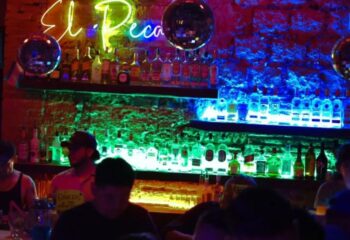 El Pecado Gay Bar in Mexico: Interior view of the bar with shelves of liquor bottles, neon lights, and disco balls. Gay travel.