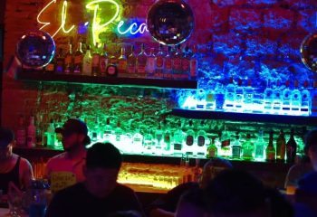 El Pecado Gay Bar in Mexico: Interior view of the bar with shelves of liquor bottles, neon lights, and disco balls. Gay travel.