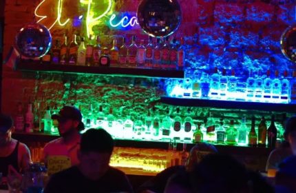 El Pecado Gay Bar in Mexico: Interior view of the bar with shelves of liquor bottles, neon lights, and disco balls. Gay travel.