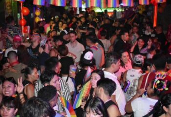 El Pecado Gay Bar in Mexico: A crowded scene with many people, rainbow flags, and balloons. Nightlife for gay men's travel advice.