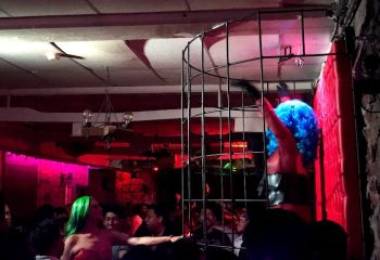 Nightlife at El Pecado Gay Bar in Mexico. Drag queen in cage, green-haired dancer, and crowd. Gay travel advice, gay bar scene.