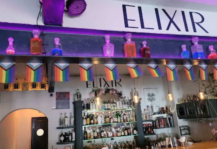 Elixir Mixology Bar interior in Puerto Vallarta. Gay party spot with rainbow flags, liquor bottles, and stylish decor. Nightlife scene.