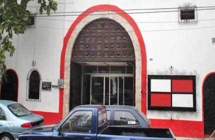 Elizabeth Taylor Theater, Puerto Vallarta. White building with red trim, arched doorway, and cars parked in front. Gay cruising spot.
