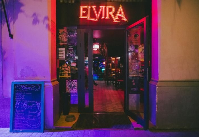 Entrance to Elvira Cafe, a gay bar in Barcelona. Neon sign above the door. Menu board on the left. Interior visible through open door.