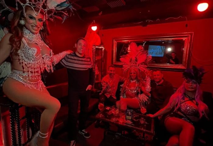 Elvira Cafe Gay Bar in Barcelona: Drag queens pose with patrons in the red-lit gay bar. Gay travel advice for Barcelona nightlife.