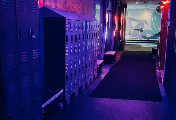 Entourage Las Vegas gay cruising venue interior. Lockers line a corridor with neon lighting, a mural, and a dark carpet.