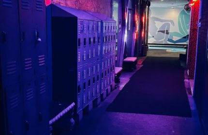 Entourage Las Vegas gay cruising venue interior. Lockers line a corridor with neon lighting, a mural, and a dark carpet.