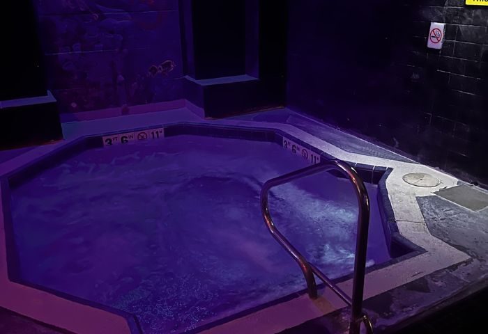 Entourage Las Vegas gay cruising: A dark, indoor hot tub with purple lighting & a metal handrail. No smoking sign visible on the wall.