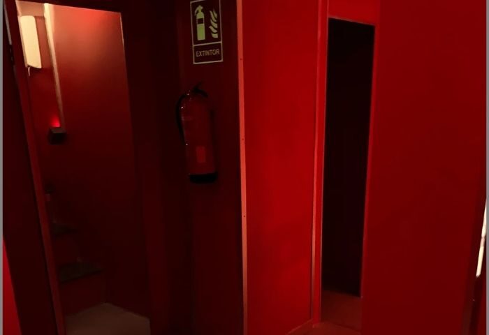 Interior of Erotic Palace, a gay cruise club in Madrid. Red walls, a fire extinguisher, and a dark doorway create an intimate atmosphere.