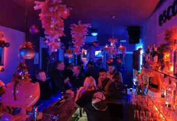 Escape Bar, a gay nightclub in Benidorm. Interior view with patrons at the bar, festive decorations, and blue lighting. Nightlife scene.