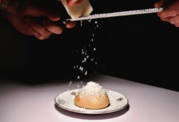 Euforia Bar Milan: Hands grating cheese over a bun on a plate. A culinary experience for gay men traveling in Milan, Italy.