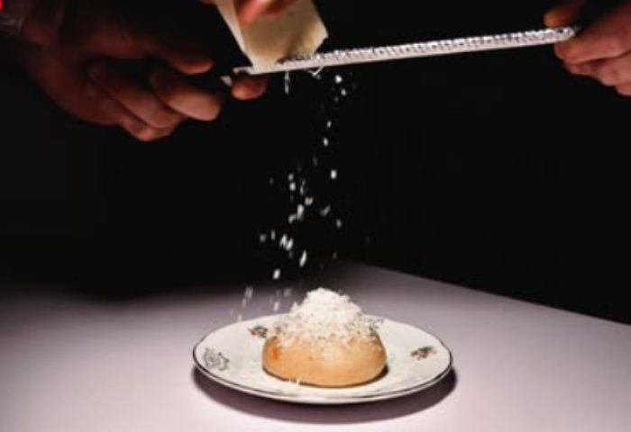 Euforia Bar Milan: Hands grating cheese over a bun on a plate. A culinary experience for gay men traveling in Milan, Italy.
