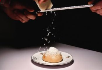 Euforia Bar Milan: Hands grating cheese over a bun on a plate. A culinary experience for gay men traveling in Milan, Italy.